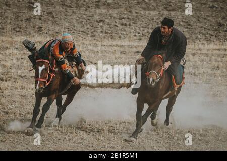 Taschkurgan, China - September 2019: Tadschikische Pferdeleute ziehen während des traditionellen Buzkashi-Spiels Ziegenkörper und reiten schnell laufende Pferde Stockfoto