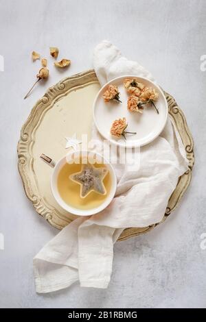 Eine Tasse Tee auf einem Vintage-Tablett und einige getrocknete Rosen auf dem Teller Stockfoto