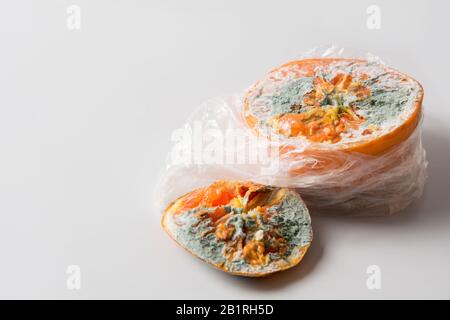 Hässliche Form orange in Zellophanverpackung auf grau. Nahaufnahme. Unsachgemäße Lagerung von Obst. Stockfoto