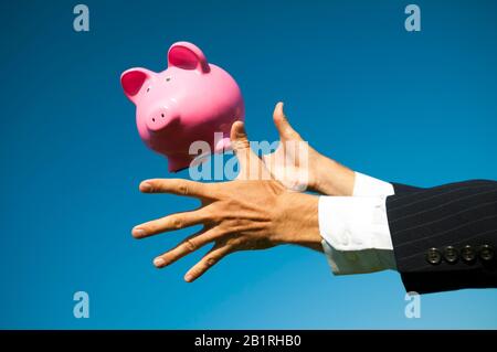 Hände von unkenntlich Geschäftsmann zu erreichen, fangen ein Sparschwein fallen von den strahlend blauen Himmel Stockfoto