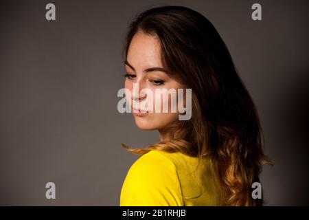 Porträt der schönen jungen kaukasischen Frau in gelbem T-Shirt über dunkelgrauem Hintergrund Stockfoto