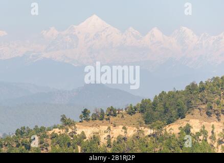 Die Panchachuli-Reihe sichtbar durch den Dunst über den von Bäumen gesäumten Hügeln aus dem Himalaya-Dorf Kausani in Uttarakhand, Indien. Stockfoto