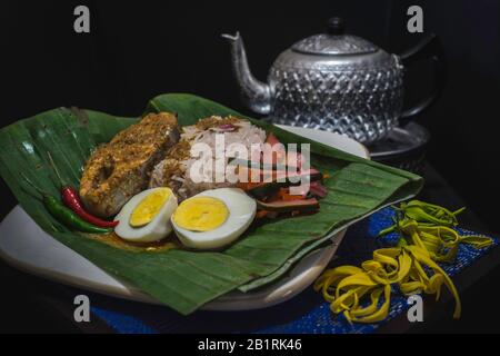 Traditioneller malaysischer Nasi-Dolch oder Reis, der in Kokosmilch gedünstet wird, wird mit Fischcurry und gekochten Eiern auf einem grünen Blatt serviert Stockfoto