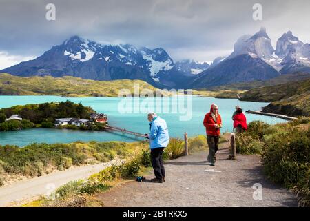 Touristen über dem Lake Pehoe und der Pehoe Lodge im Nationalpark Torres del Paine, Patagonien, Chile, deren Gewässer durch glaziale Felsblumen verfärbt sind Stockfoto