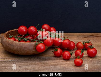 Frisch tomatilos auf schwarzem Hintergrund von der Seite gesehen, auf Holzoberfläche; Frisch ganz und rot tomatillos geschnitten (halbiert) auf schwarzem Grund gesehen f Stockfoto