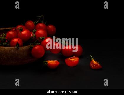 Frisch tomatillos auf schwarzem Hintergrund von der Seite betrachtet, Frisch ganz und geschnitten (halbiert) rot tomatillos auf schwarzem Hintergrund von oben betrachtet - Essen ST Stockfoto