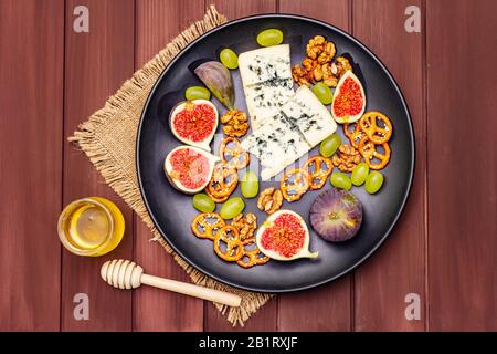 Käseplatte mit Blaukäse, Honig, Walnüsse, Feigen, Trauben, Brezeln. Traditionelle gesunde Appetithäppchen, Snacks und Antipasti. Holzbretter Hintergrund, Vint Stockfoto