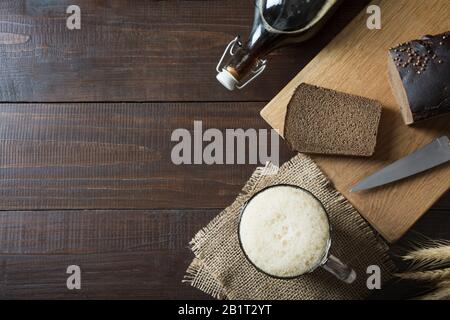 Russisches traditionelles Getränk fermentierter Kvass aus Roggenbrot im speziellen Halbliter-Becher auf dunklem Hintergrund. Ansicht von oben. Leerzeichen für Text. Stockfoto