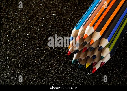 Gruppe von Bleistiften, die auf schwarzem Sand liegen. Bunte Bleistifte. Stockfoto