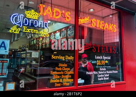 New York City, USA - 3. August 2018: Zeigen Sie mit einem Kellner, der auf die Straße in Manhattan, New York City, USA blickt, den Laden von Tads Broiled Steaks an Stockfoto