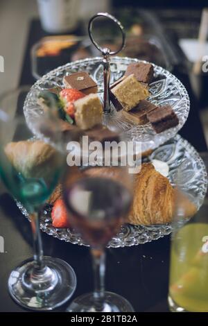 Ein Kuchenständer mit Erdbeeren und Kuchen, der im Vordergrund eine Cocktailbrille zeigt Stockfoto