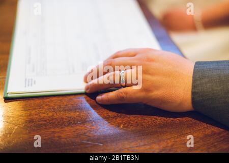 Eine neue weiße Goldhochzeit an der Hand eines Bräutigam mit Hochzeitsregistrierungsbuch im Hintergrund Stockfoto