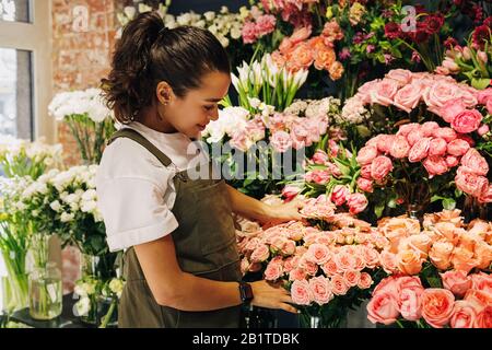Frau Floristin trägt Schürze, die auf Blumen in ihrem Laden schaut Stockfoto