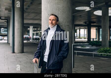 Stilvoller älterer Mann, der draußen am Flughafenterminal steht und wegschaut Stockfoto