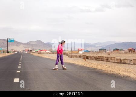 Mongolia Ulgii 2019-05-05 mongolisches Mädchen in bunter Kleidung reitet pinke Inline-Skates auf der Straße im asiatischen Dorf auf dem Hintergrund der Berge. Konzept von Stockfoto