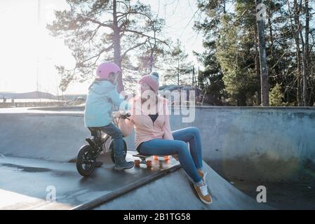 Frau spielt mit ihrer Tochter in einem Skatepark draußen in der Sonne Stockfoto
