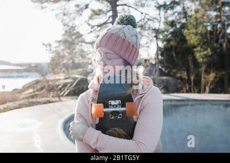 Frau saß mit geschlossenen Augen und hielt ihr Skateboard in einem Skatepark Stockfoto