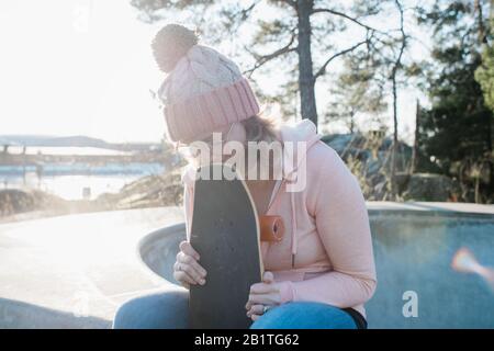 Frau, die sich auf ihr Skateboard lehnt, während sie in einem Skatepark bei Sonnenuntergang ist Stockfoto