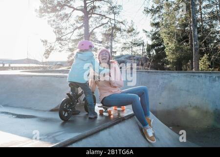 Mutter und ihre Tochter lachen während sie in einem Skatepark spielen Stockfoto