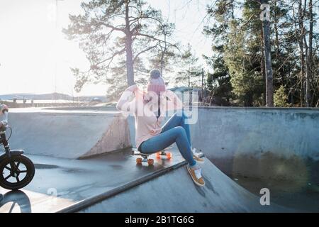 Frau saß auf einem Skateboard in einem Skatepark lächelnd in der Sonne Stockfoto