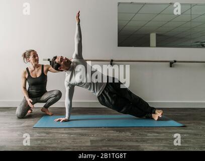 Weibliche Personal Trainer trainiert männlichen Kunden tun eine seitwärts Plank Stockfoto