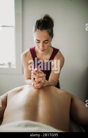 Weibliche Massagetherapeutin verwendet Unterarme, um auf dem Rücken des männlichen Patienten zu arbeiten Stockfoto