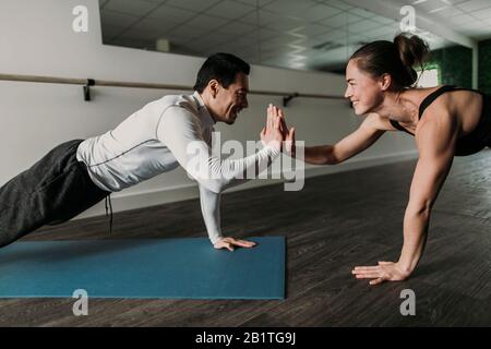 Männliche und weibliche Freunde High Five während Liegestütze im Fitnessstudio Stockfoto