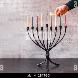 Bild einer Hand, die Kerzen auf Menorah für Chanukka anzündet. Stockfoto