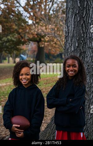 Porträt lächelnder Schwestern mit American Football im Park Stockfoto