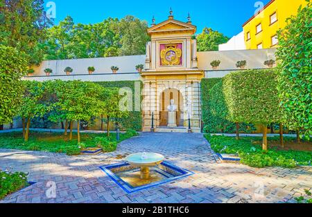 Sevilla, SPANIEN - 1. OKTOBER 2019: Der Innenhof des Alcazar-Palastes mit beschnittenen Pflanzen, einem kleinen Brunnen und der Büste des Königs Pedro I. und dem Mantel des Arms Stockfoto