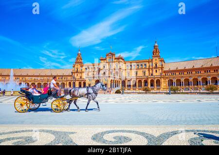 Sevilla, SPANIEN - 1. OKTOBER 2019: Touristen fahren mit offener Pferdekutsche entlang der Plaza de Espana und genießen die beeindruckende Architektur des andalusischen Mudeja Stockfoto