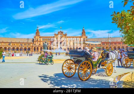 Sevilla, SPANIEN - 1. OKTOBER 2019: Die Linie der Touristenpferdewagen im Schatten der Bäume des Parks Maria Luisa mit Blick auf die Plaza de Espana, Stockfoto