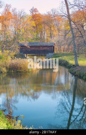 Überdachte Brücke im Herbst mit Reflexionen in einem Bach Stockfoto