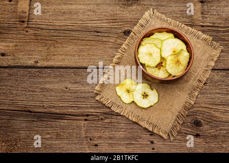 Getrocknete Apfelscheiben in der Schüssel. Fruchtsnack, gesundes Esskonzept. Sacktuch, alter Holztafeln Hintergrund, Draufsicht, Kopierraum Stockfoto