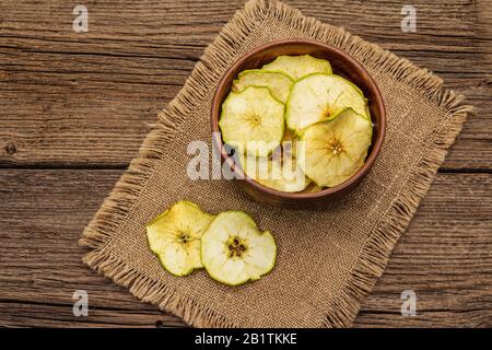 Getrocknete Apfelscheiben in der Schüssel. Fruchtsnack, gesundes Esskonzept. Sacktuch, alter Holztafeln Hintergrund, Draufsicht, Kopierraum Stockfoto