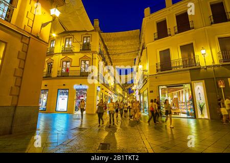 Sevilla, SPANIEN - 1. OKTOBER 2019: Die lokale Jugend geht nachts entlang der Einkaufsstraßen, vorbei an hellen Vitrinen zahlreicher Boutiquen und Geschäfte Stockfoto