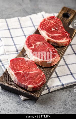 Aus dem Tenderloin auf Holzschneidebrett schneiden sich drei Stück traditionelles dünnes Steak. Das Steak hat gute Marmorierung, schöne gleichmäßige Form und ist zart Stockfoto