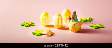 Frohe Ostern. Osterdekorationen in Form von gelben Ziereiern, Blumen und einem Keramikhuhn auf pinkfarbenem Hintergrund. Oster-Feiertag-Konzept Backg Stockfoto