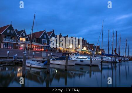 Blick auf den Hafen von Volendam und Yacht, Boote und Segelboote anchored, Volendam, Niederlande. Marine mit beleuchteten Häusern und blauem Himmel. Stockfoto