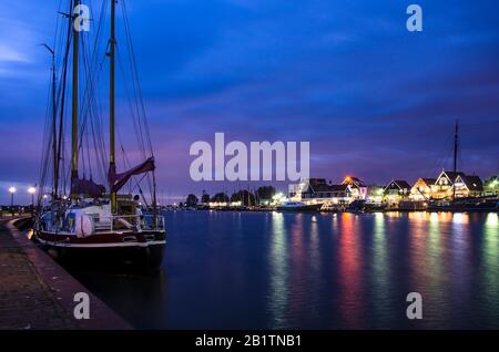 Blick auf den Hafen von Volendam und Yacht, Boote und Segelboote anchored, Volendam, Niederlande. Marine mit beleuchteten Häusern und blauem Himmel. Stockfoto