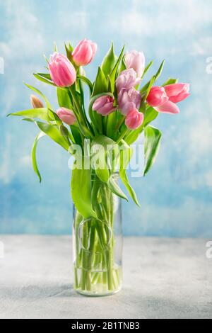 Blumenstrauß aus rosa und lila Tulpen in ein Glas Vase auf blauem Hintergrund Stockfoto