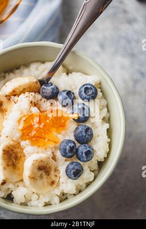 Nahaufnahme von Schüsselfrühstück mit Milchreis-Porridge mit Bananen, Blaubeere, Zimt- und Orangenjam, cremigem Reis-Pudding oder französischem Riz au Lait in einem Bogen Stockfoto