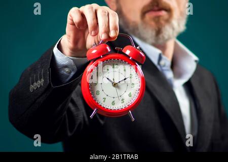 Bärtiger Geschäftsmann im Anzug mit rotem Wecker. Zeitmanagement Konzept Stockfoto