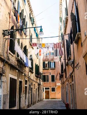 Wäsche trocknet auf dem Draht im Hof in der schmalen Straße zwischen hohen Wänden, Venedig, Italien. Wäscherei, die aus einer typisch venetianischen Fassade hängt. Stockfoto