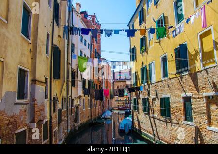 Wäscherei, die aus einer typisch venetianischen Fassade, Italien, hängt. Enge Kanalstraße mit bunten Gebäuden und Booten in Venedig und Kleidung trocken an einem Seil Stockfoto