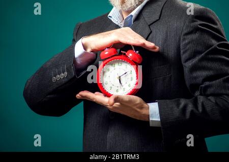 Bärtiger Geschäftsmann im Anzug mit rotem Wecker. Zeitmanagement Konzept Stockfoto