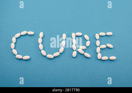 Medizinische weiße Pillen, Tabletten, die das Wort Heilung auf blauem Hintergrund bilden. Medizin, Drogenbehandlung von Krankheiten. Konzept eines neuen chinesischen Coronavirus Stockfoto