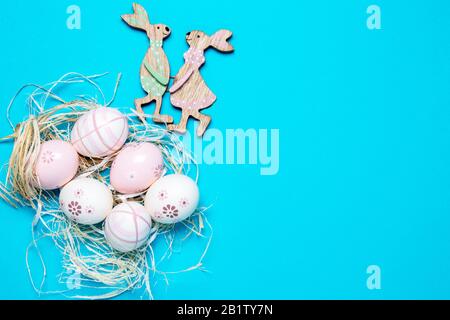 Vorlage für die Osterkarte. Die Draufsicht über bunte Eier mit Strohhalm und ein paar holz-osterhasen-Flat lag auf blauem Grund. Großer Platz für Ihr t Stockfoto