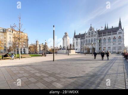 Budapest, Ungarn - 26. November 2019: Ungarische parlamentsgebäude und Park von der Seite mit Menschen an einem sonnigen Tag in der Herbstsaison, abgewinkelte Sicht. Stockfoto