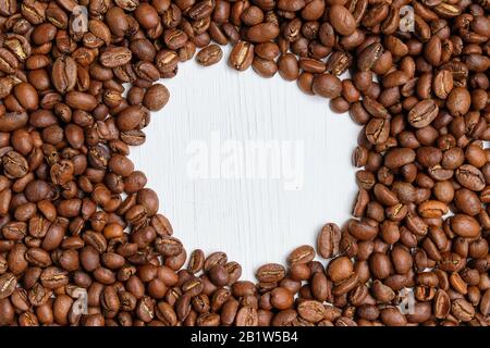 Kaffee geröstete Körner auf weißem Holzhintergrund mit Kreis. Kopierbereich. Nahaufnahme. Stockfoto